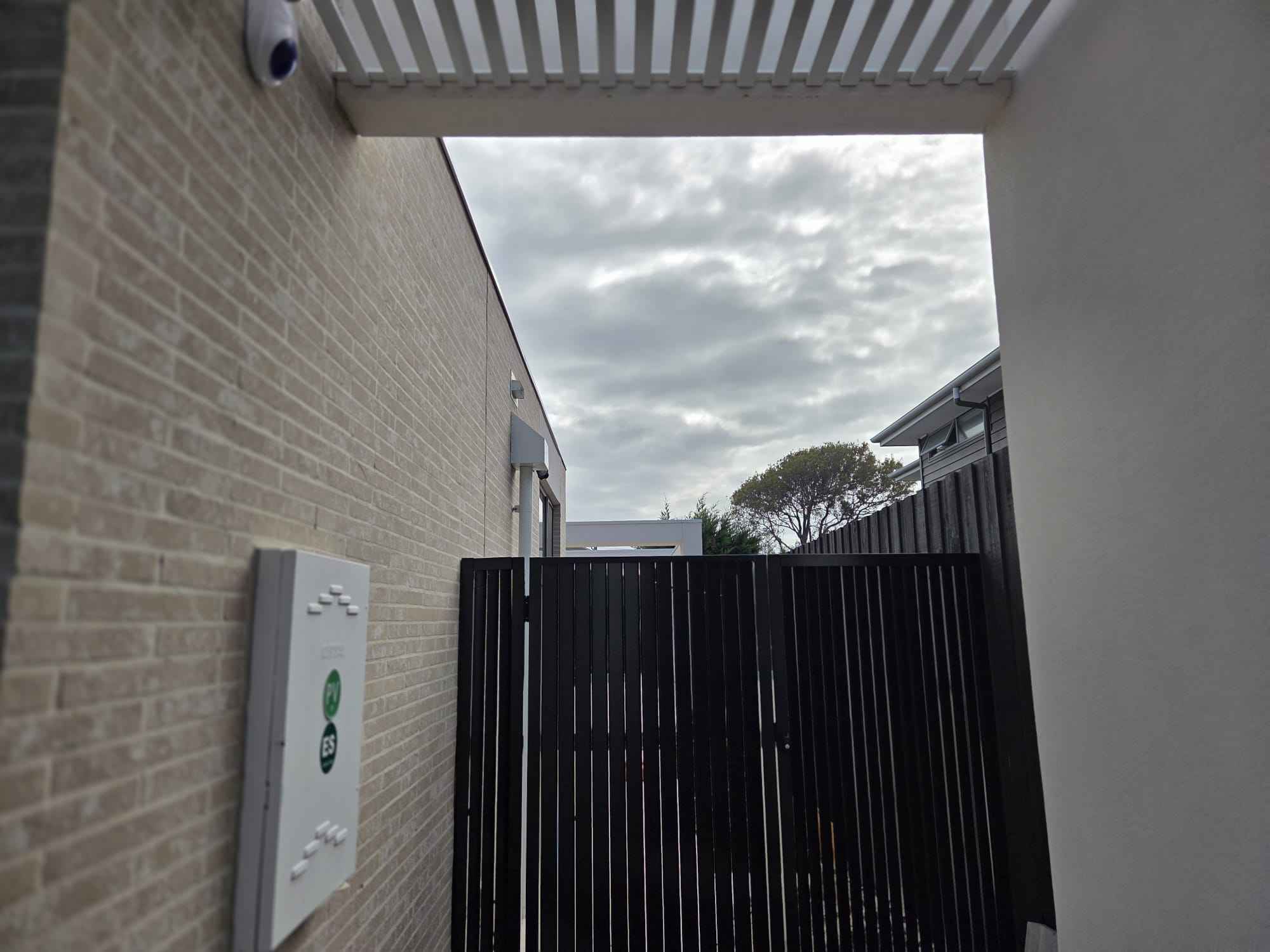 Black slat side gate and screening beside a rendered wall
