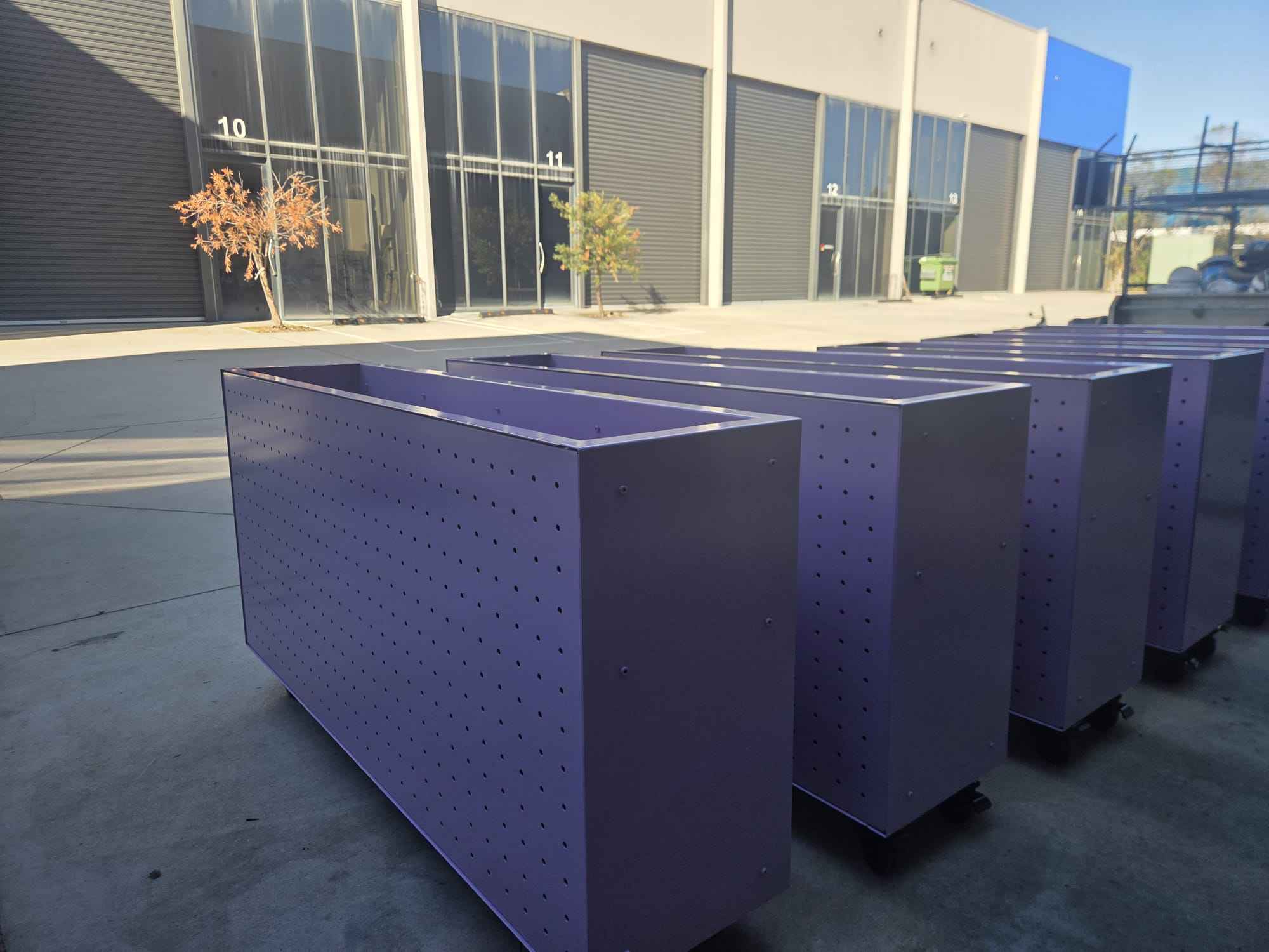 Perforated steel planter boxes lined up outside the workshop